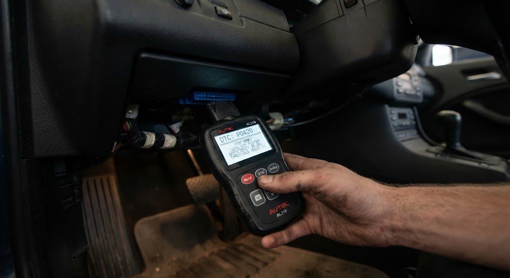 Handheld OBD-II scanner displaying a P0420 catalytic converter code, plugged into the diagnostic port of a vehicle